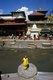 Nepal: A sadhu stands in front of the Bagmati River, while a yellow shrouded body awaits cremation on the far bank, Pashupatinath, Kathmandu